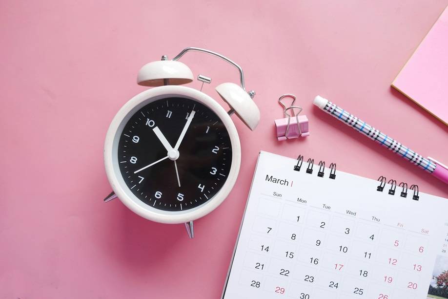 Alarm clock, pen, and planner on pink desk