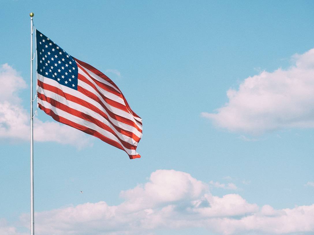 American flag on flagpole against blue sky with white clouds