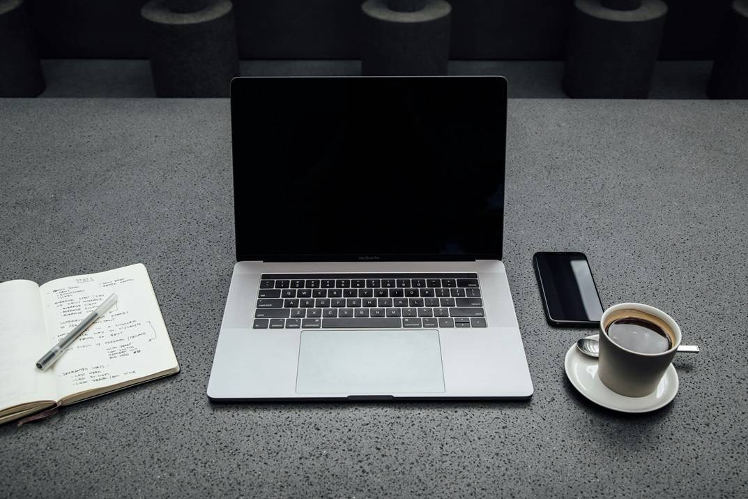 Laptop, notebook, cell phone, coffee cup on gray table