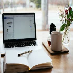 Notebook open with pen, laptop, and cup of coffee