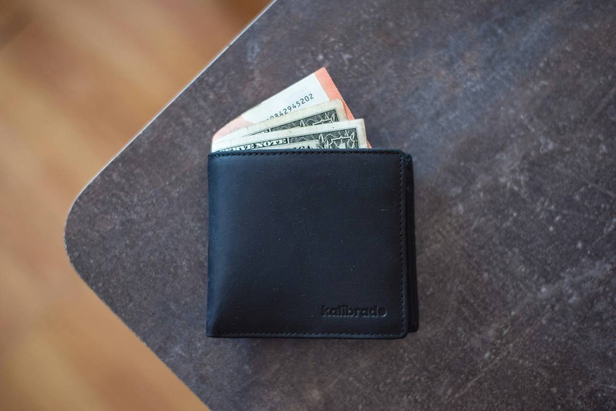 Black wallet with cash sticking out on gray table