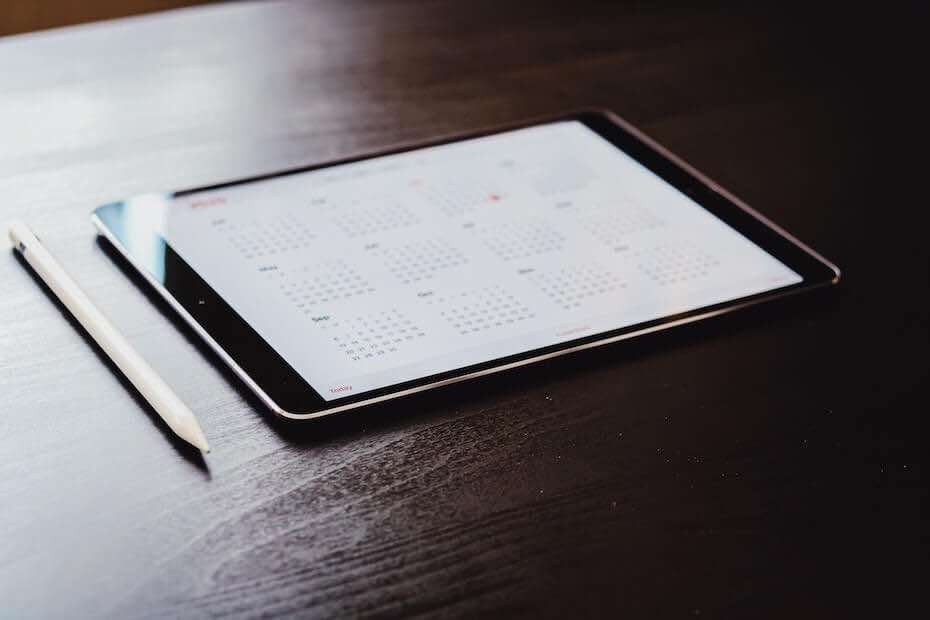 Tablet displaying a calendar and a pencil on a wood table