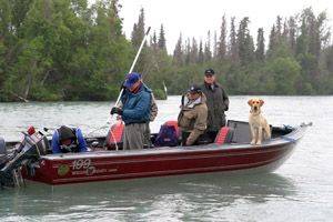 Three people and a yellow dog in a red boat fishing on the Kenai River.