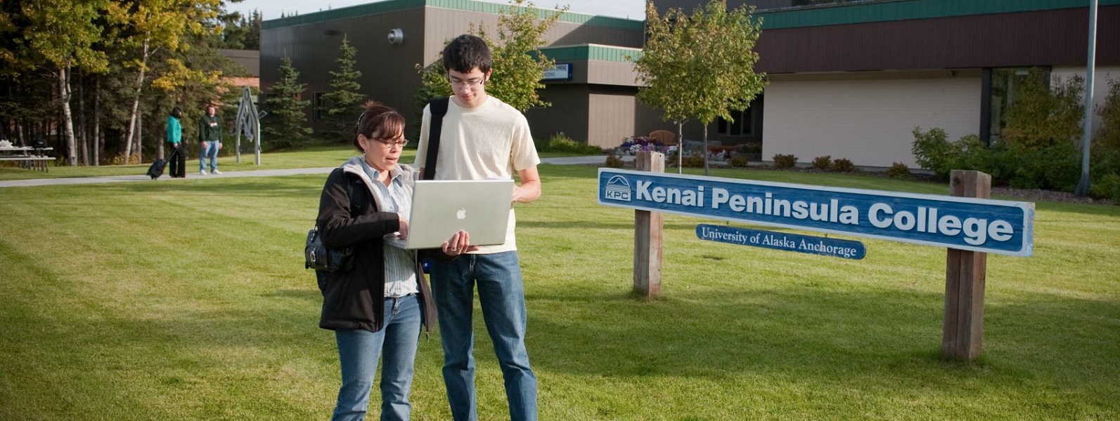 Two students (female and male) in front of the KPC sign (on the front lawn) at the Kenai River Campus