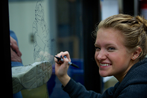 Smiling female student writing on glass window